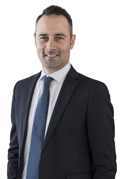 Ein Mann in einem dunklen Anzug mit weißem Hemd und Krawatte lächelt in die Kamera.