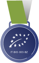 Medaille mit grünem Band, blauem Kreis und weißen Sternen in Blattform, darunter Text "IT-BIO-003-BZ".